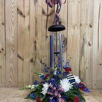Chime on stand with fresh flowers added. Can be made in many different variations and color schemes. Depending on season or whether it is made for a lady or man. Please call in to the shop and speak to one of our talented designers to place an order for a piece as pictured.